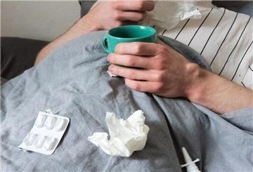  Ein Mann liegt mit Taschentüchern, Teetasse, Nasenspray und Tabletten im Bett.