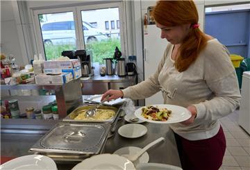 Eine Frau steht in der Küche und füllt Essen auf einen Teller. 