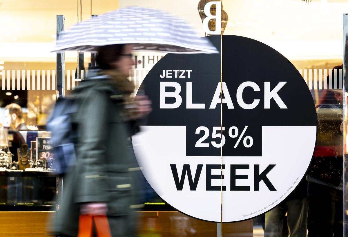 Prime Days, Cyber Monday, Black Friday - mit diesen Tipps Rabattfallen erkennen Eine Person mit einem Regenschirm geht an einem Geschäft vorbei, das für Angebote im Rahmen der Black Week wirbt.