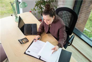 Eine Frau sitzt am Schreibtisch und blättert in Steuer-Unterlagen.
