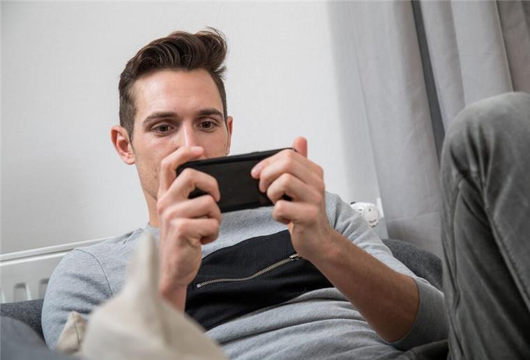Vom Bildschirm zur Auszeit: So gelingt der Digital Detox Ein Mann sitze auf einer Couch und hängt vor dem Handy