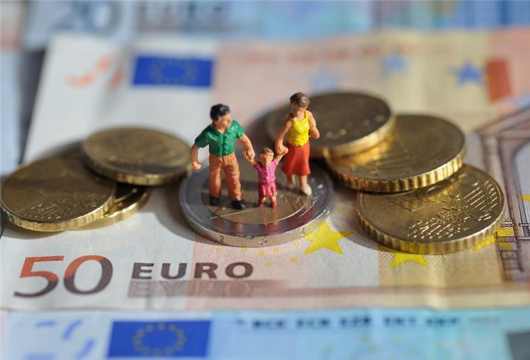 Sparkassen: Viele Haushalte verbrauchen ihr ganzes Einkommen Ein Paar mit einem Kind steht auf einer Zwei-Euro-Münze, die auf einem 50-Euro-Schein liegt.