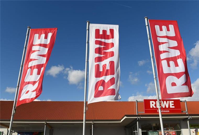 Nach jahrelangem Lieferstopp: Beliebte Kultprodukte kehren bei Rewe in die Regale zurück Mehrere Rewe-Flaggen wehen vor einer Filiale im Wind.