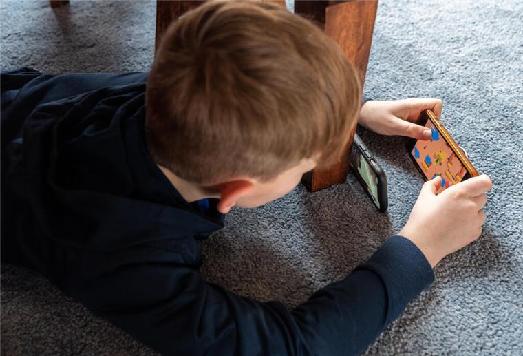 Glücksspielrisiko in Online-Games: Lootboxen stehen unter Beschuss Ein Junge liegt auf dem Fußboden und spielt ein Spiel an seinem Handy. Glücksspiel im Gaming: Niedersachsen fordert strengere Regeln für bestimmte Videospiele.