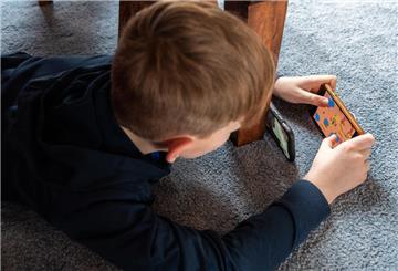 Ein Junge liegt auf dem Fußboden und spielt ein Spiel an seinem Handy. Glücksspiel im Gaming: Niedersachsen fordert strengere Regeln für bestimmte Videospiele.