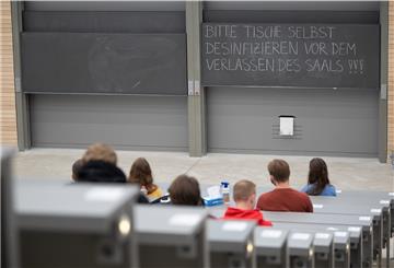 Studierende mit Mund- und Nasenmaske sitzen in der Begrüßungsveranstaltung für Studierende im ersten Semester an einer Universität vor einer Tafel auf der «Bitte Tische selbst desinfizieren vor dem Verlassen des Saals» steht.