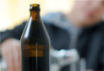 Hinter einer leeren Bierflasche gießt ein Jugendlicher Schnaps in ein Glas.