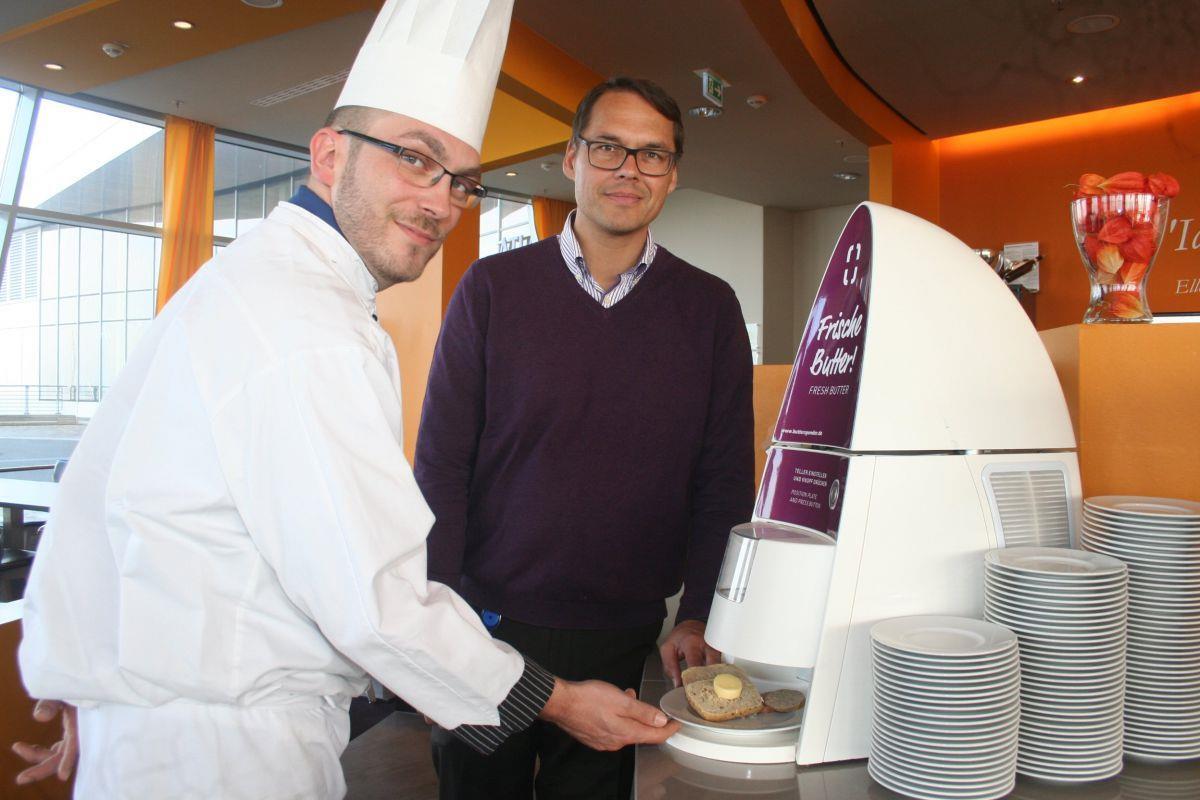 Vincent Hackstein und Tim Oberdieck zeigen, wie die Butterdosiermaschine funktioniert. Die Menge reicht genau für eine Hälfte des eigens dafür entwickelten Brötchens.
