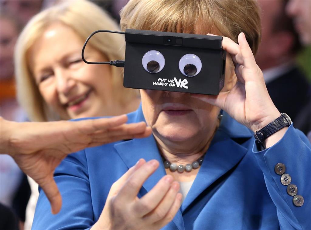 Volle Durchblick: Bundeskanzlerin Angela Merkel beim Stand von ifm electronic auf der Hannover Messe. In der Hand hält sie eine VR Brille vors Gesicht.
