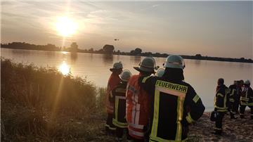 Vom östlichen Ufer der Weser aus beobachten diese Feuerwehrleute, wie ein Rettungshubschrauber die Wasseroberfläche absucht.