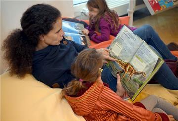 Eine Mutter sitzt mit ihren Töchtern bei der Jugendbuchmesse "Kibum - total tierisch" in einem Sitzkissen und schaut sich mit einem der Mädchen ein Buch über Dinosaurier an. 