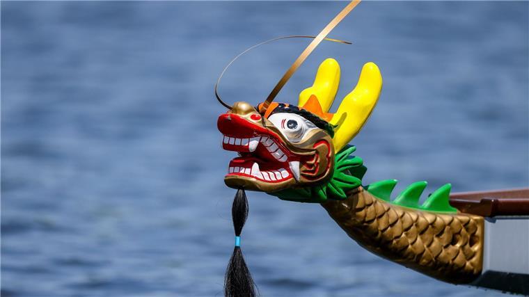 Mit der Trommel Paddler anfeuern Vorn am Boot hängt ein bunter Drachenkopf.