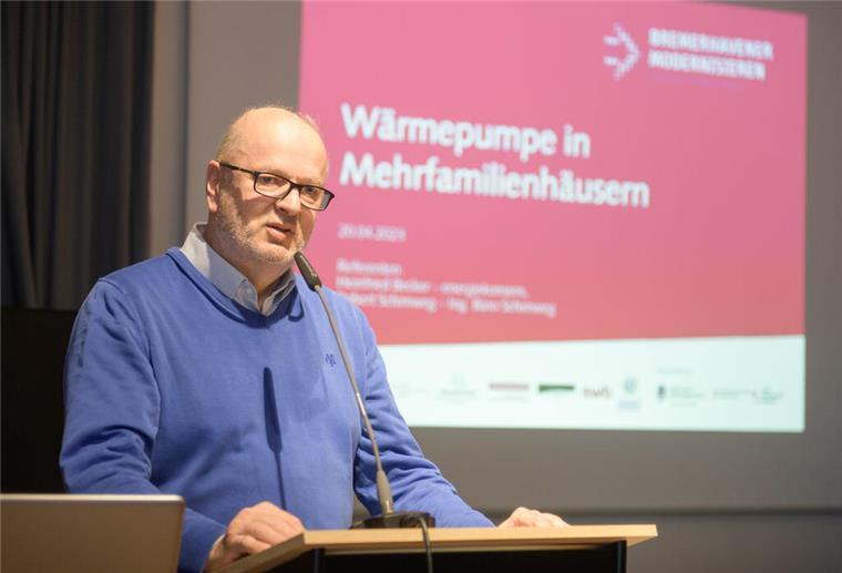 Ein Referent hält einen Vortrag zum Thema "Wärmepumpen in Mehrfamilienhäusern". Das Thema ist im Hintergrund auf einer Leinwand zu sehen.