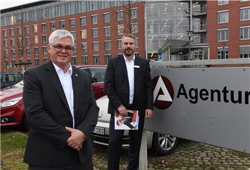 Wolfgang Mögenburg und Frank Westphal stehen neben dem Schild mit der Aufschrift Agentur für Arbeit