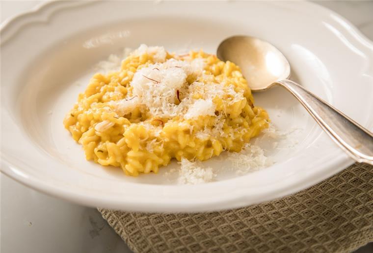 Mögliche Arsenbelastung: Reis vor dem Kochen gründlich abspülen Ein Risotto aus Reis liegt auf einem weißen Teller. Darüber ist Käse gestreut, daneben liegt ein Löffel.