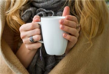 Eine Frau hält eine weiße Tasse mit einem Teebeutel in der Hand.
