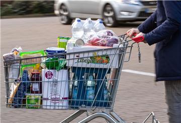 Ein Einkaufswagen mit Lebensmitteln und Produkten des täglichen Bedarfs wird über den Parkplatz eines Supermarkts geschoben. 