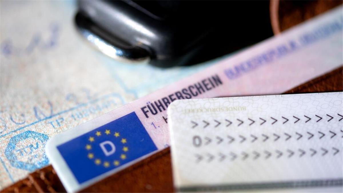 Ein Führerschein, ein Autoschlüssel, ein Personalausweis und eine Zulassungsbescheinigung liegen auf einem Portemonnaie.
