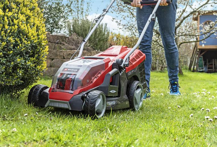 Ein roter Rasenmäher mäht einen Garten.