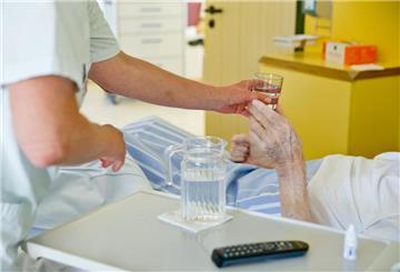 Ein Pfleger reicht einer Heimbewohnerin ein Glas Wasser.