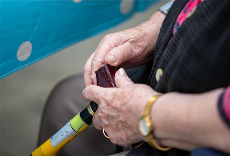Digitale Lösungen für die Pflegeplatzsuche Eine Seniorin sitzt mit ihrem Gehstock im Garten im Pflegeheim.