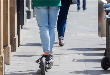 Ein Mann fährt mit einem E-Scooter auf dem Gehweg.