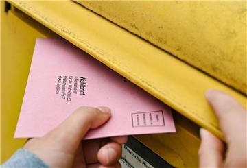 Eine Person wirft ihre Briefwahlunterlagen in einen Postkasten der Deutschen Post.