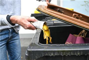 Eine Frau wirft in Zeitungspapier gewickelte Bananenschalen in eine Mülltonne für den Biomüll. Wer sich nicht an die Entsorgungsregeln für Müll hält, riskiert saftige Bußgelder. Diese können bis 25.000 Euro hoch sein.