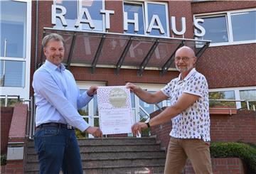 Zwei Männer halten vor dem Beverstedter Rathaus ein Plakat in die Kamera.