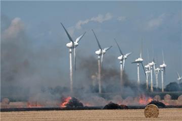 Windräder sind hinter den brennenden Strohballen zu erkennnen.