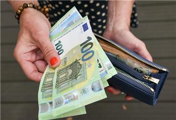 Eine Frau hält eine mit mehreren Geldscheinen gefüllte Geldbörse in einer Hand, darunter Hundert-, Fünfzig- und Zwanzig-Euro-Scheine, und einige Geldscheine in der anderen Hand.