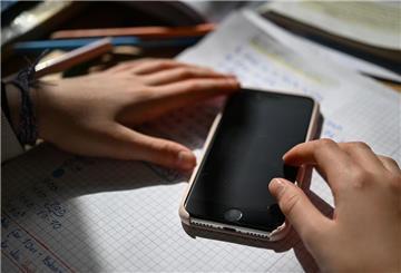 Ein Schulkind sitzt an einem Schreibtisch mit Schulmaterialien und hält ein Smartphone in den Händen. Das Smartphone beeinflusst uns mehr als wir denken. 