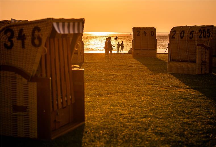 Wurster Nordseeküste: Gästekarten soll auch andernorts gelten Im Vordergrund stehen Strandkörbe auf einem Grünstrand, im Licht des Sonnenuntergangs sind Silhouetten von Menschen zu sehen.
