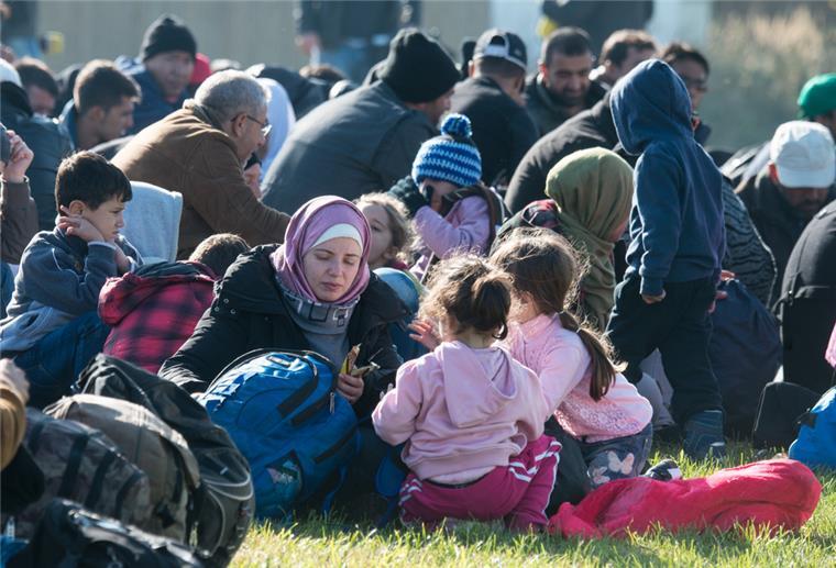 Bremen: Leichtbauhallen für Geflüchtete werden aufgestellt Geflüchtete sitzen auf einer Wiese