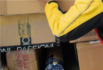 Ein Paketzusteller stellt ein Paket in ein Fahrzeug der Deutschen Post DHL.